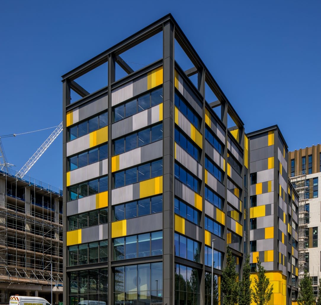 MGAC Behind the Build Preston Barracks. The image shows the exterior of the Plus X innovation hub building, which is several stories tall and composed of glass, and grey and yellow panels.