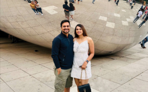 MGAC Senior Scheduler Nilesh Jain is pictured in front of the Chicago Bean, with his partner, a woman wearing a grey dress. Nilesh is wearing a navy shirt and khaki pants.